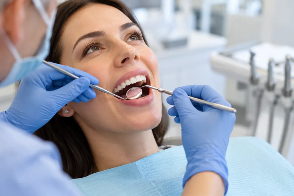 Dentysta sprawdza zęby i dziąsła pacjentki przy użyciu lusterka stomatologicznego.
